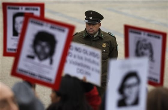 A police officer looks on Wednesday as people hold portraits of family members who were dissidents killed during the dictatorship of former Gen. Augusto Pinochet. They are demonstrting outside La Moneda government palace in Santiago, Chile. The Roman Catholic Church handed Chile's President Sebastian Pinera a petition for massive pardons that include military officials who committed crimes against humanity during Pinochet's dictatorship.